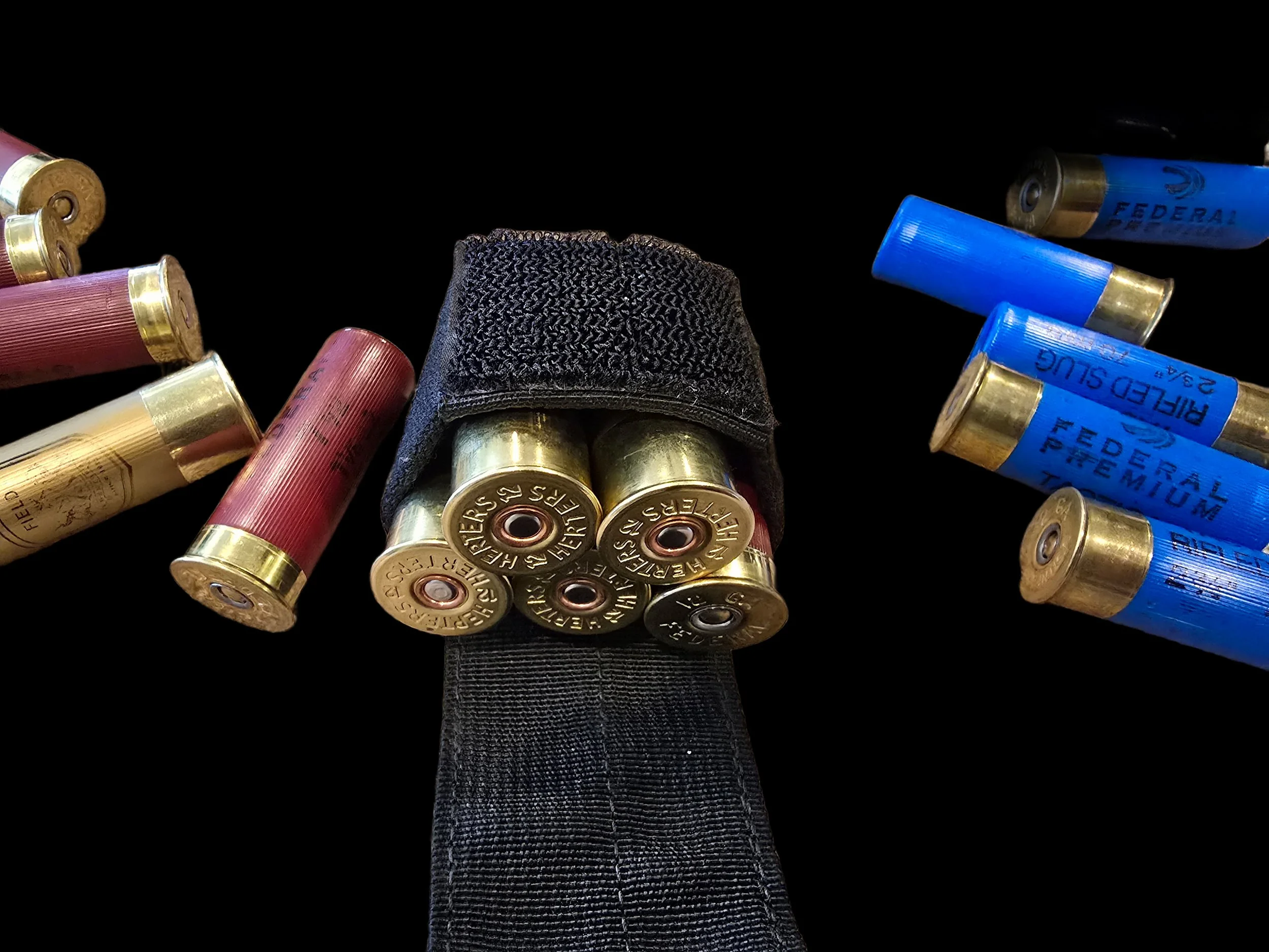 Several shotgun cartridges, some inside a black fabric holder, with red and blue shells, arranged on a black background.