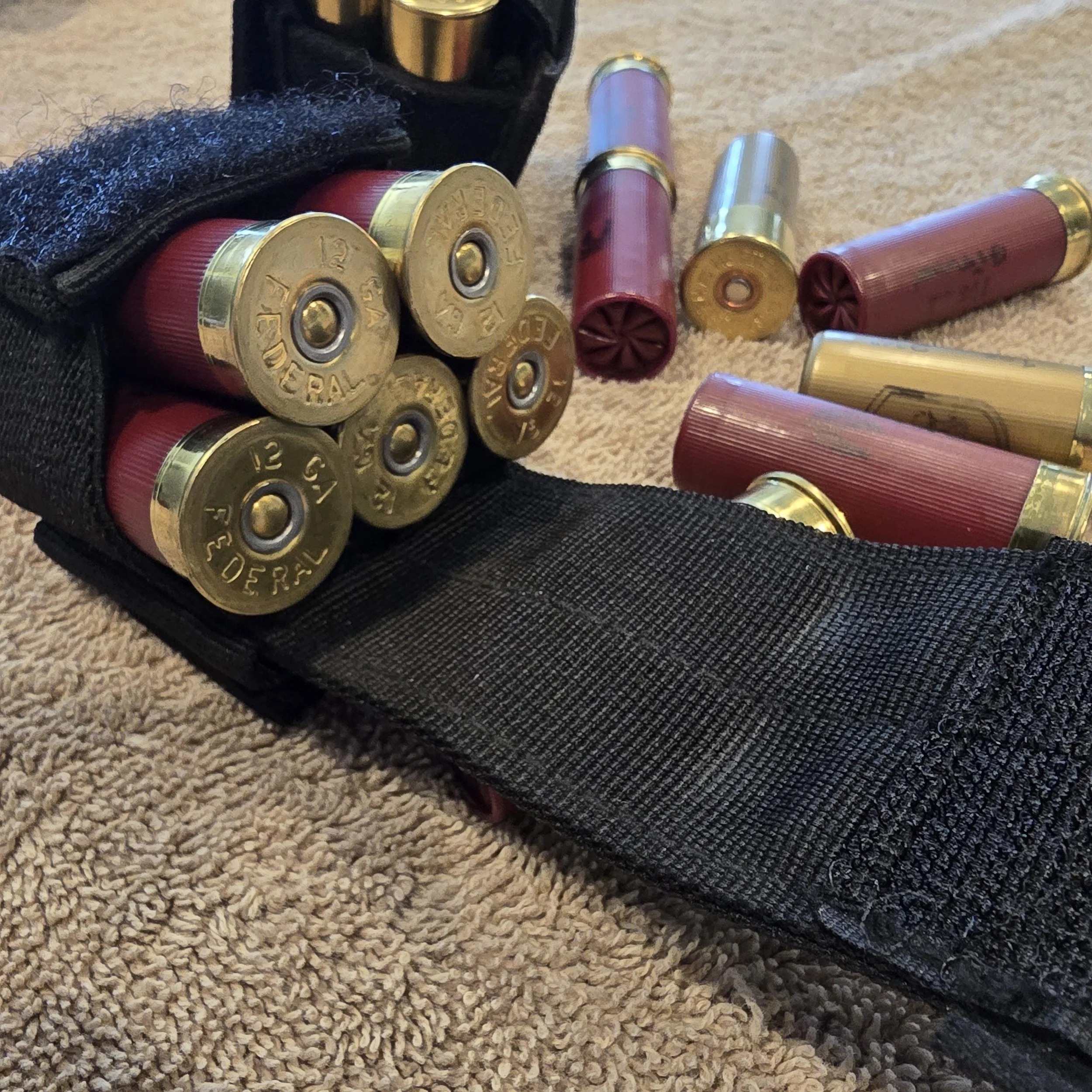 A black tactical pouch containing a number of shotgun shells, some scattered on a beige carpet.