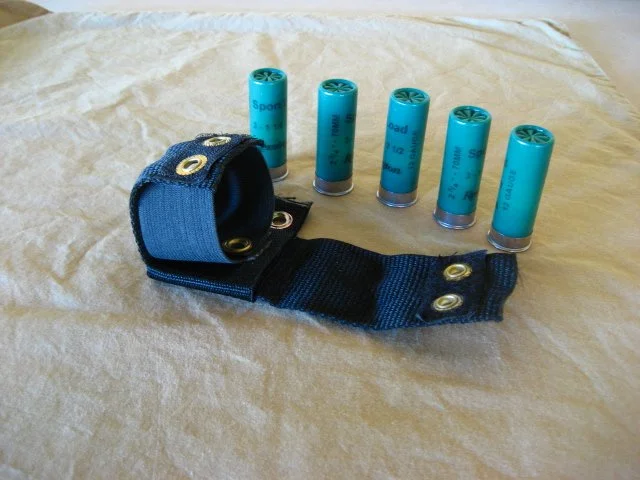 A black and blue shotgun shell holder with six empty blue shotgun shells on a light-colored surface.