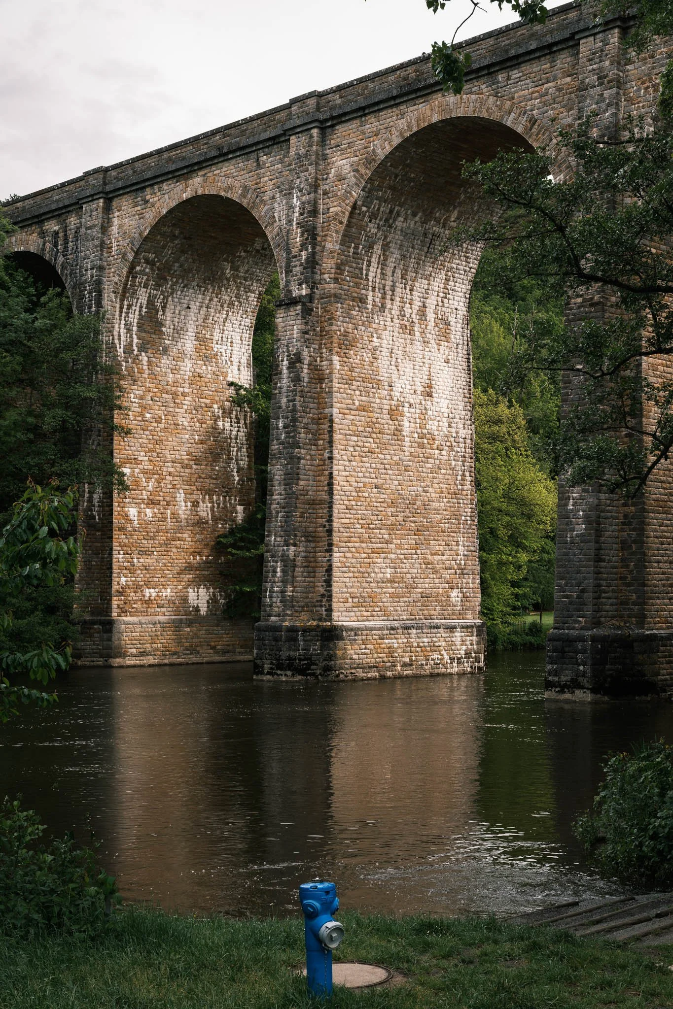 Suisse Normande - Un pont en pierre sur une rivière, entouré d'arbres verts.
