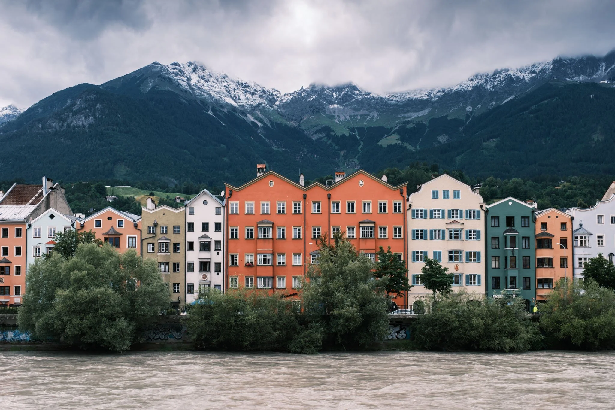 Tyrol - Ville colorée d'Innsbruck avec des bâtiments multicolores au bord d'une rivière, avec des montagnes enneigées en arrière-plan. Reportage outdoor, mise en valeur du territoire et tourisme durable par Guillaume Donsimoni