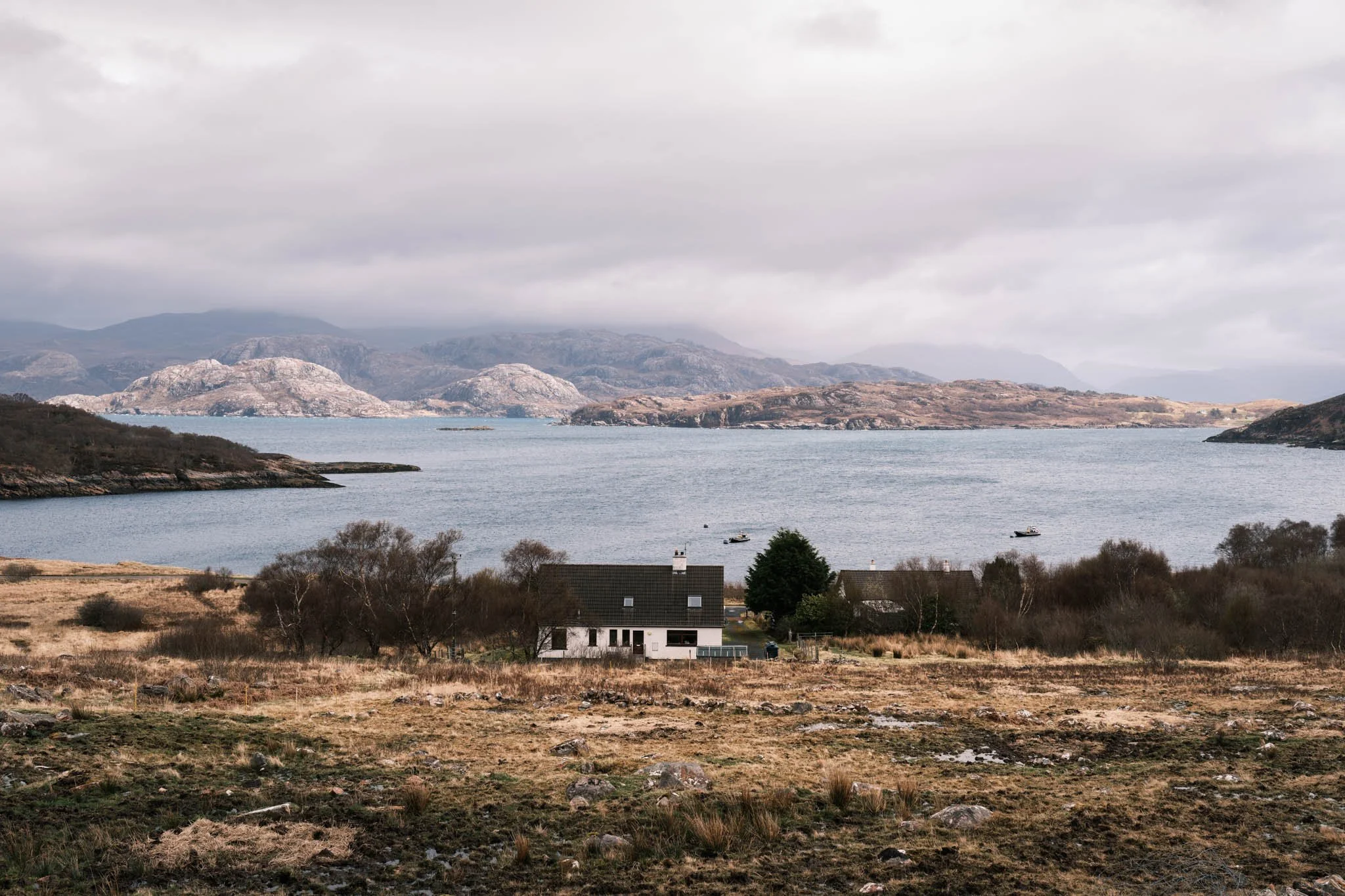 Highland - Scotland - Paysage au bord du Loch, montagnes en arrière-plan, maison au premier plan, ciel nuageux.