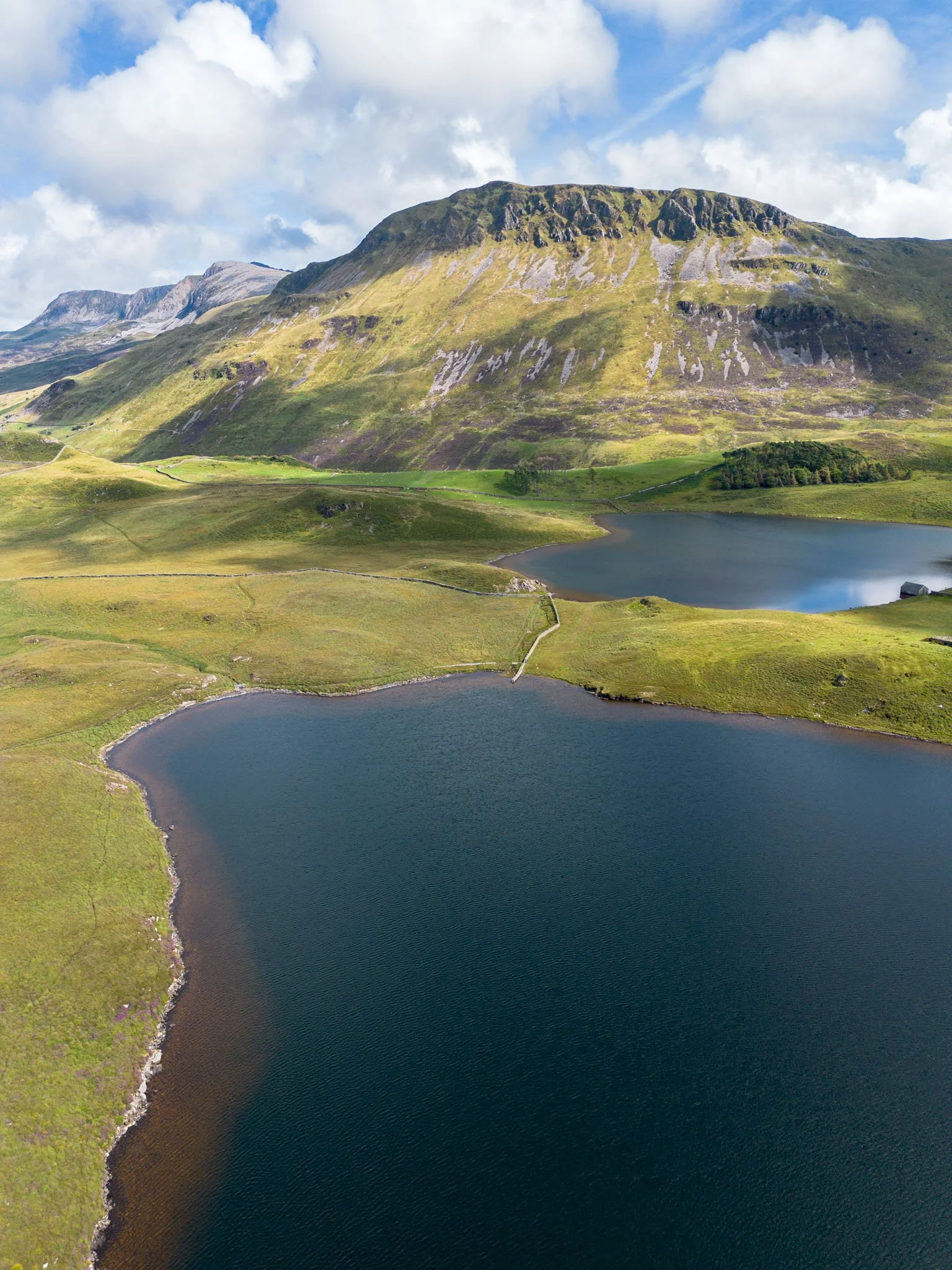 Wales - Mountainous landscape with two lakes, greenery, and a rocky peak, under a partially cloudy sky. Outdoor reportage, regional promotion, and sustainable tourism by Guillaume Donsimoni.