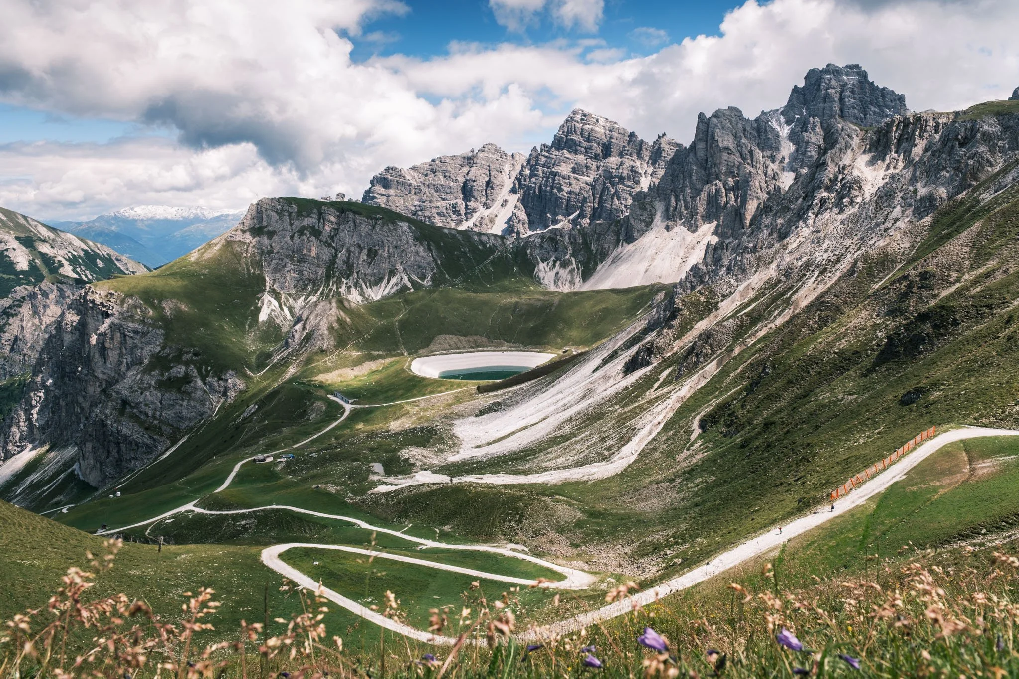 Tyrol - Paysage montagneux avec routes sinueuses, un lac artificiel, des prairies vertes et des sommets rocheux sous un ciel partiellement nuageux. Reportage outdoor, mise en valeur du territoire et tourisme durable par Guillaume Donsimoni