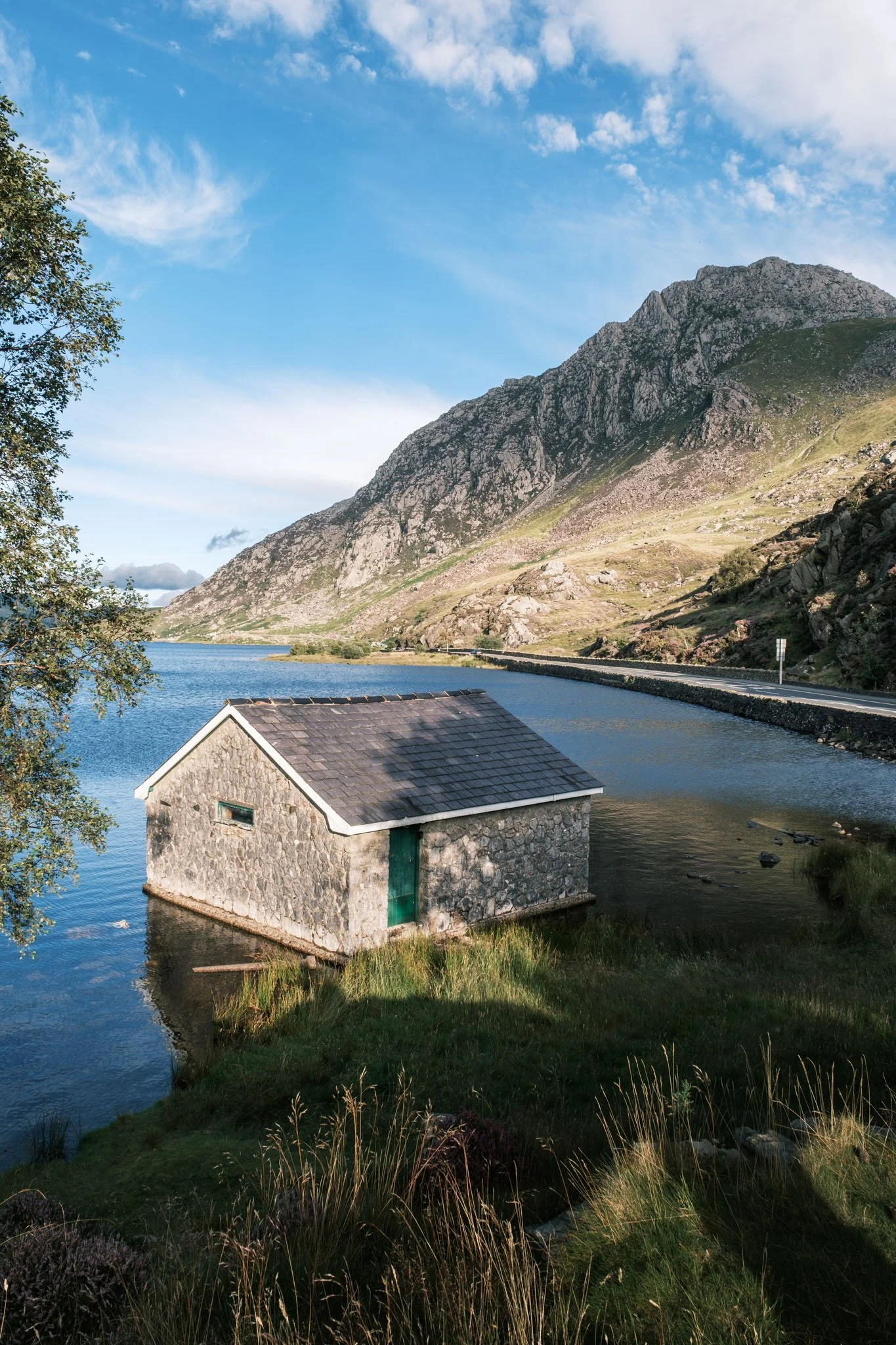 Wales - Stone cabin by a lake in a mountainous landscape with a blue sky and a few clouds. Snowdonia. Outdoor reportage, regional promotion, and sustainable tourism by Guillaume Donsimoni.
