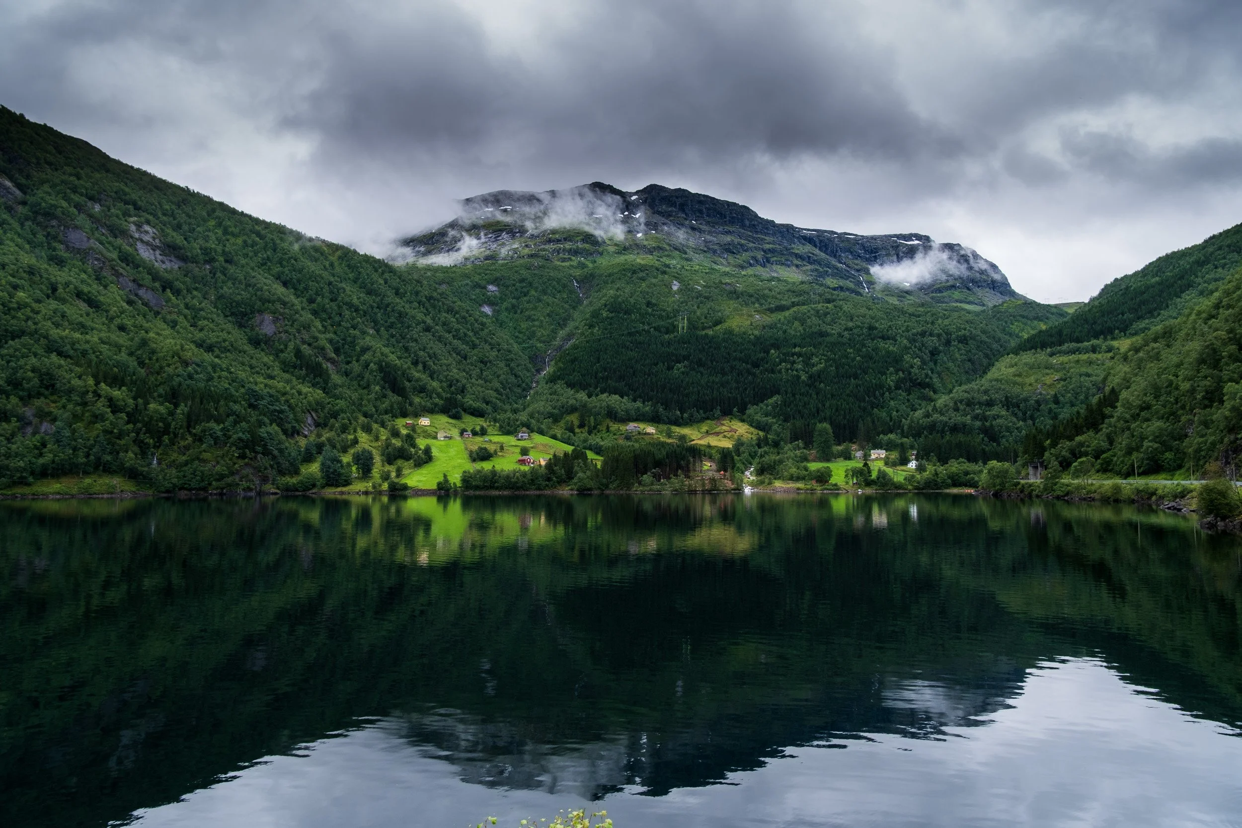 Norway: Landscape of green mountains with a lake in the foreground and small houses scattered on the hillside. Outdoor reportage, territorial promotion, and sustainable tourism by Guillaume Donsimoni.