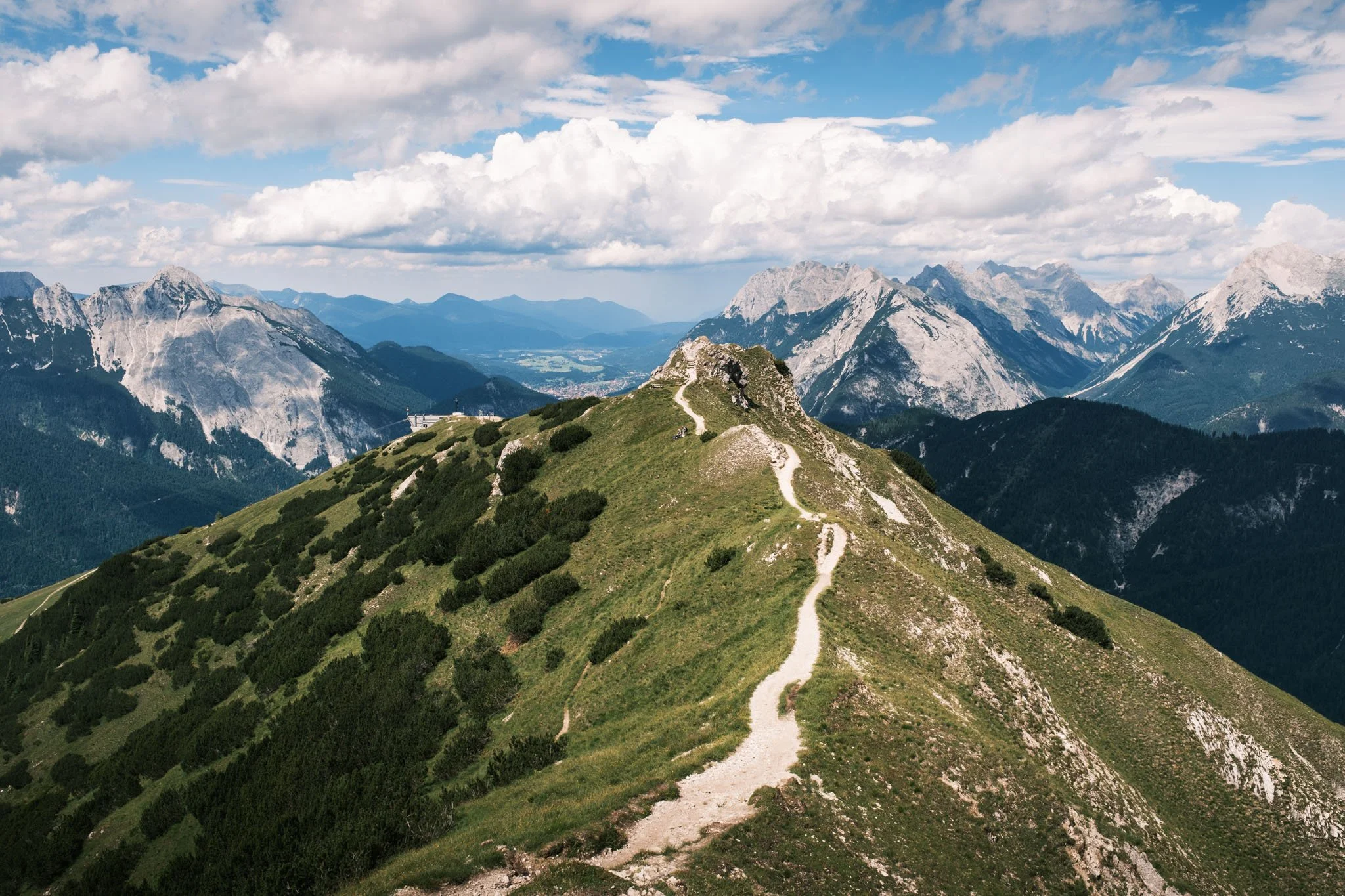 Tyrol - Chemin de randonnée sur une colline verdoyante avec des montagnes en arrière-plan sous un ciel partiellement nuageux. Reportage outdoor, mise en valeur du territoire et tourisme durable par Guillaume Donsimoni