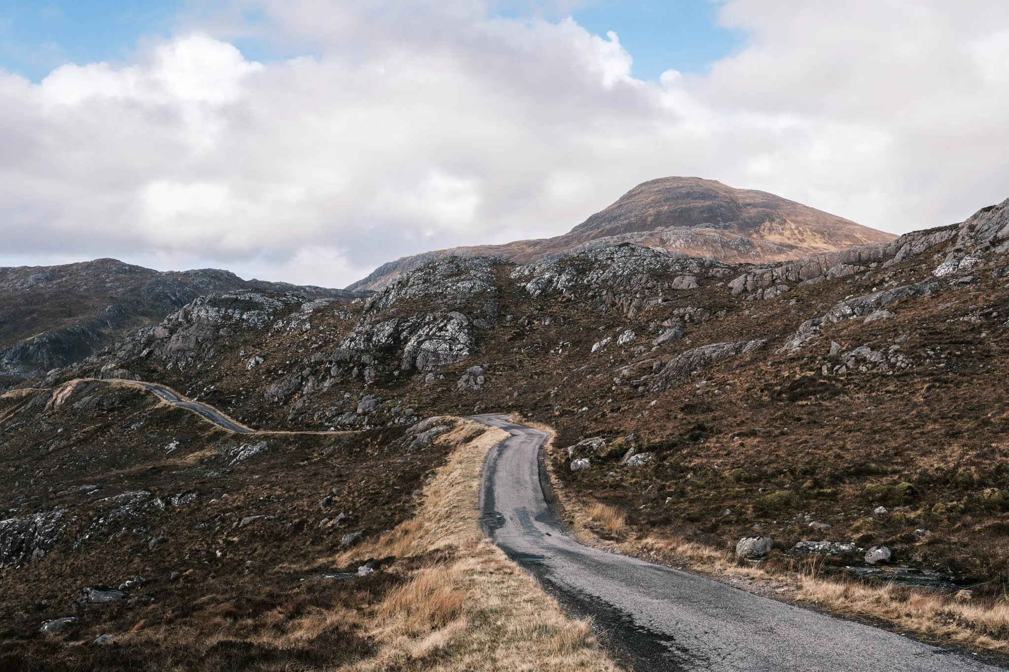 Highland - Scotland - une route sinueuse à travers des montagnes rocheuses sous un ciel nuageux.