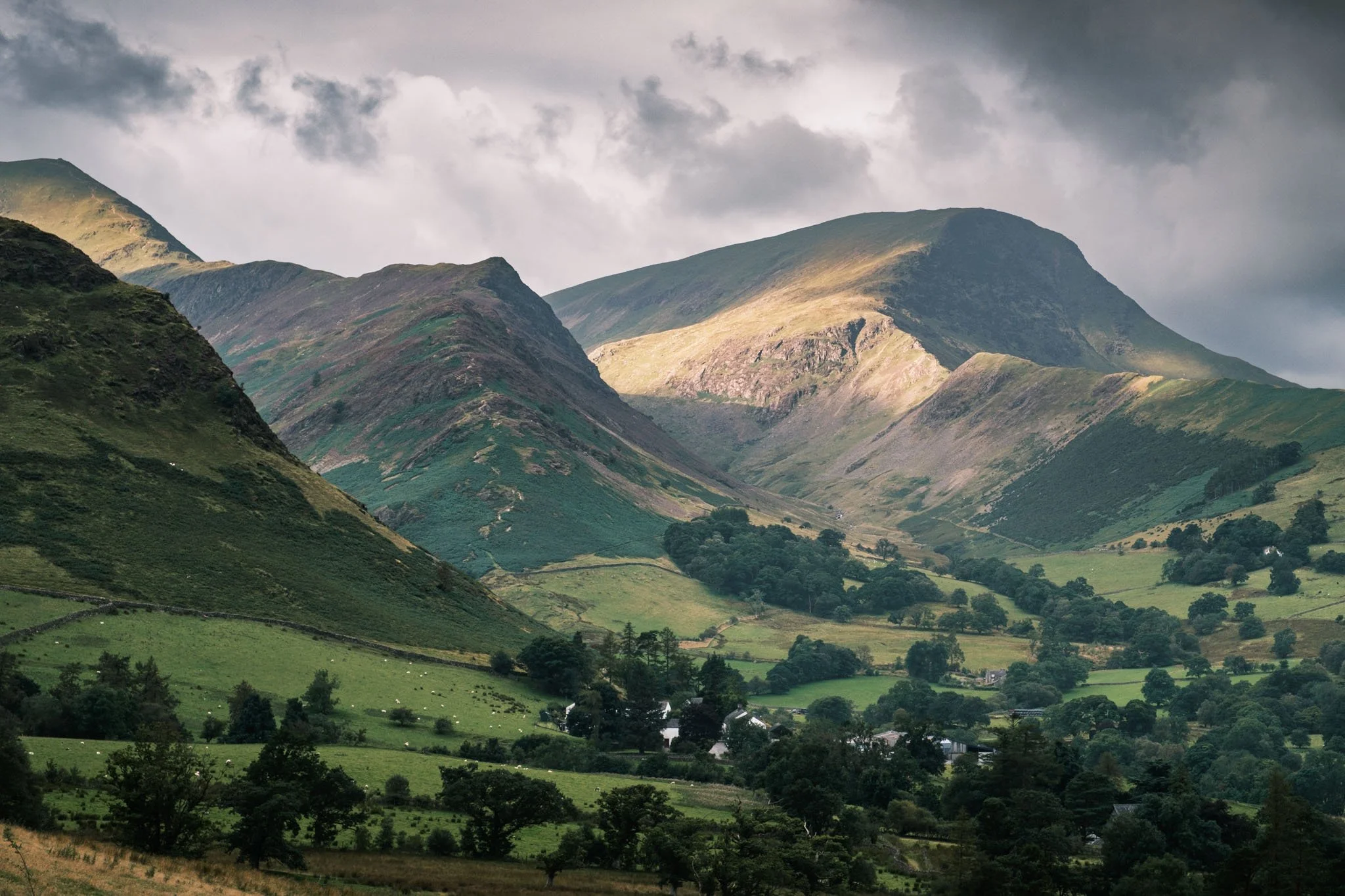 Lake District - Paysage de montagnes verdoyantes avec des collines et des vallées, quelques maisons dispersées, ciel nuageux.  Reportage outdoor, mise en valeur du territoire et tourisme durable par Guillaume Donsimoni.