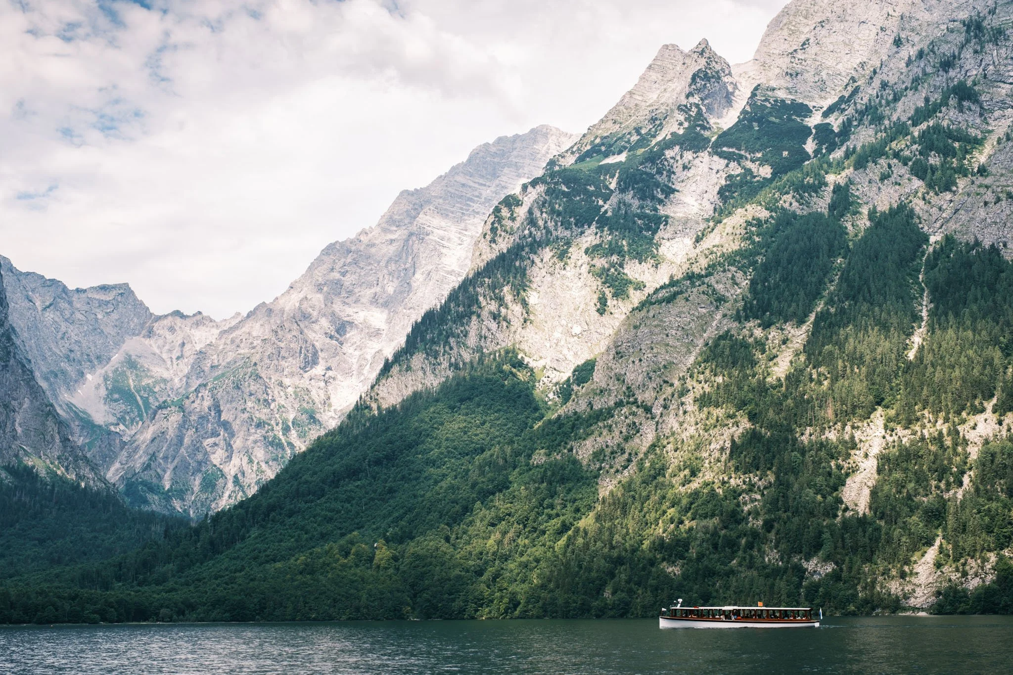 Germany - Bavière Un bateau navigue sur un lac entouré de montagnes escarpées avec des forêts verdoyantes. Reportage outdoor, mise en valeur du territoire et tourisme durable par Guillaume Donsimoni