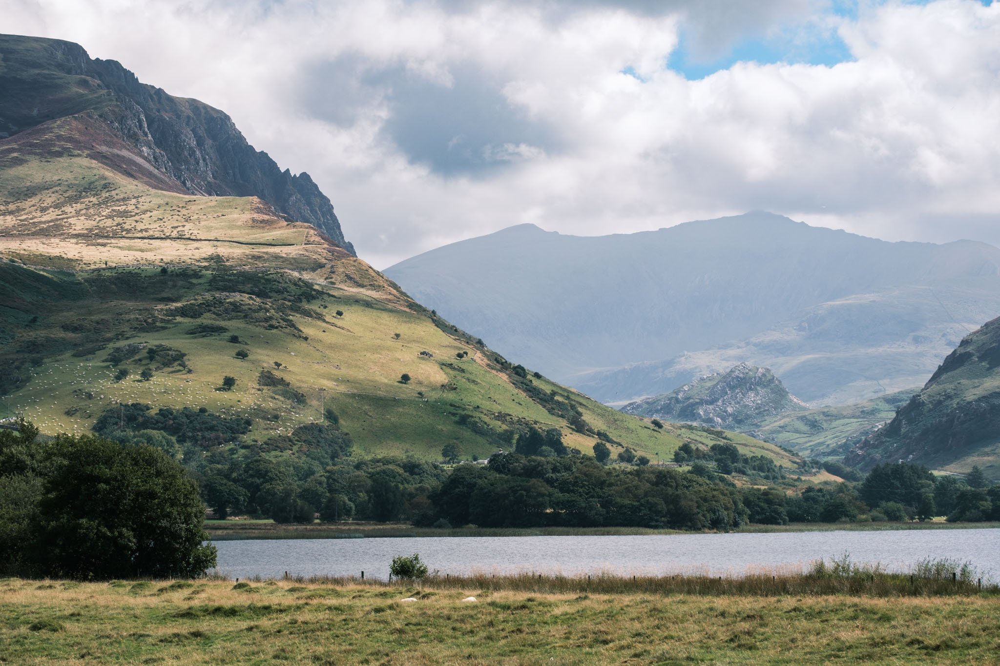 Wales - Landscape with a lake, green hills, and mountains under a cloudy sky. Outdoor reportage, regional promotion, and sustainable tourism by Guillaume Donsimoni.