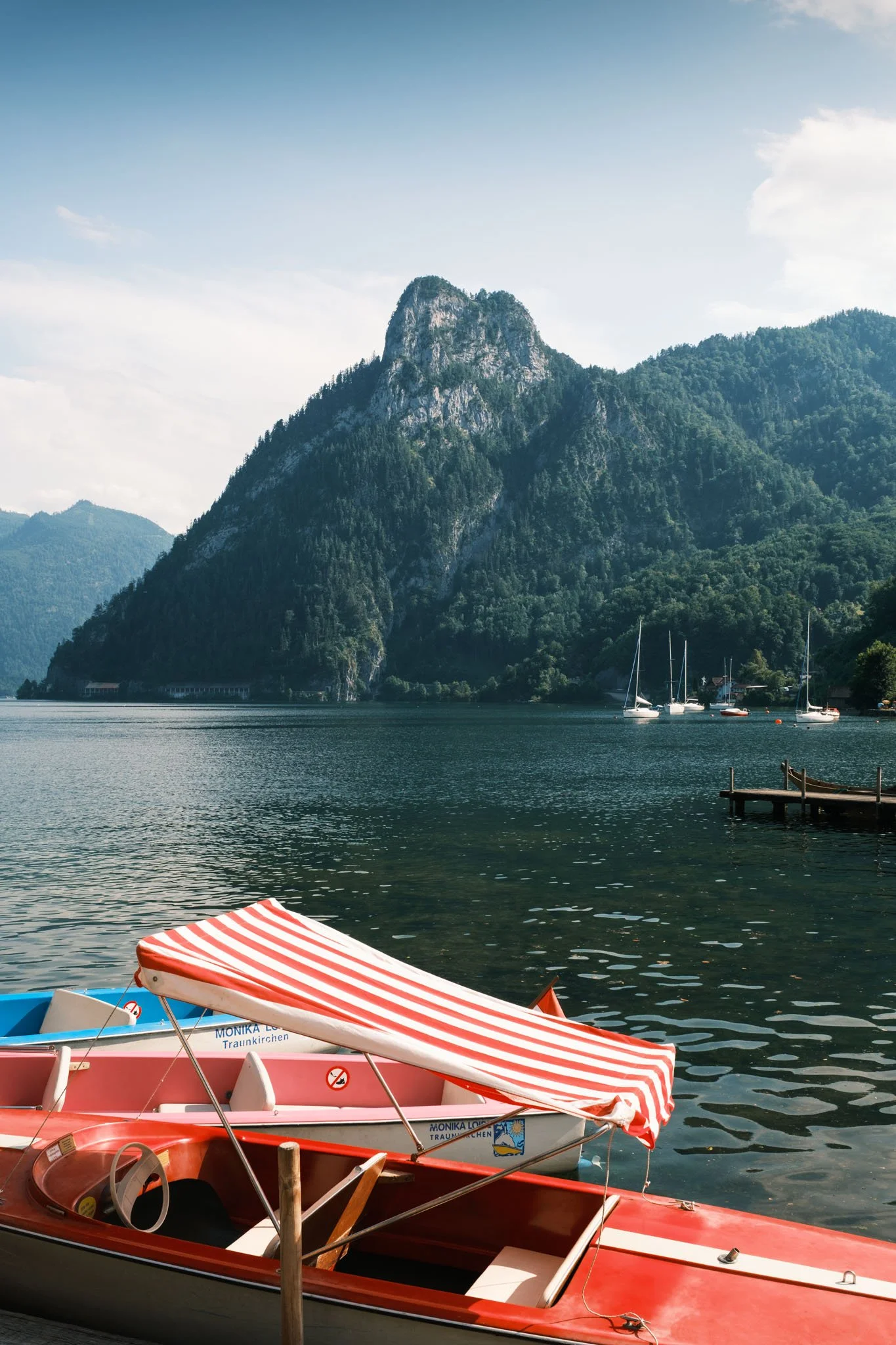 Austria - Bateaux en bois à rayures rouges et blanches au bord d’un lac entouré de montagnes verdoyantes. Reportage outdoor, mise en valeur du territoire et tourisme durable par Guillaume Donsimoni