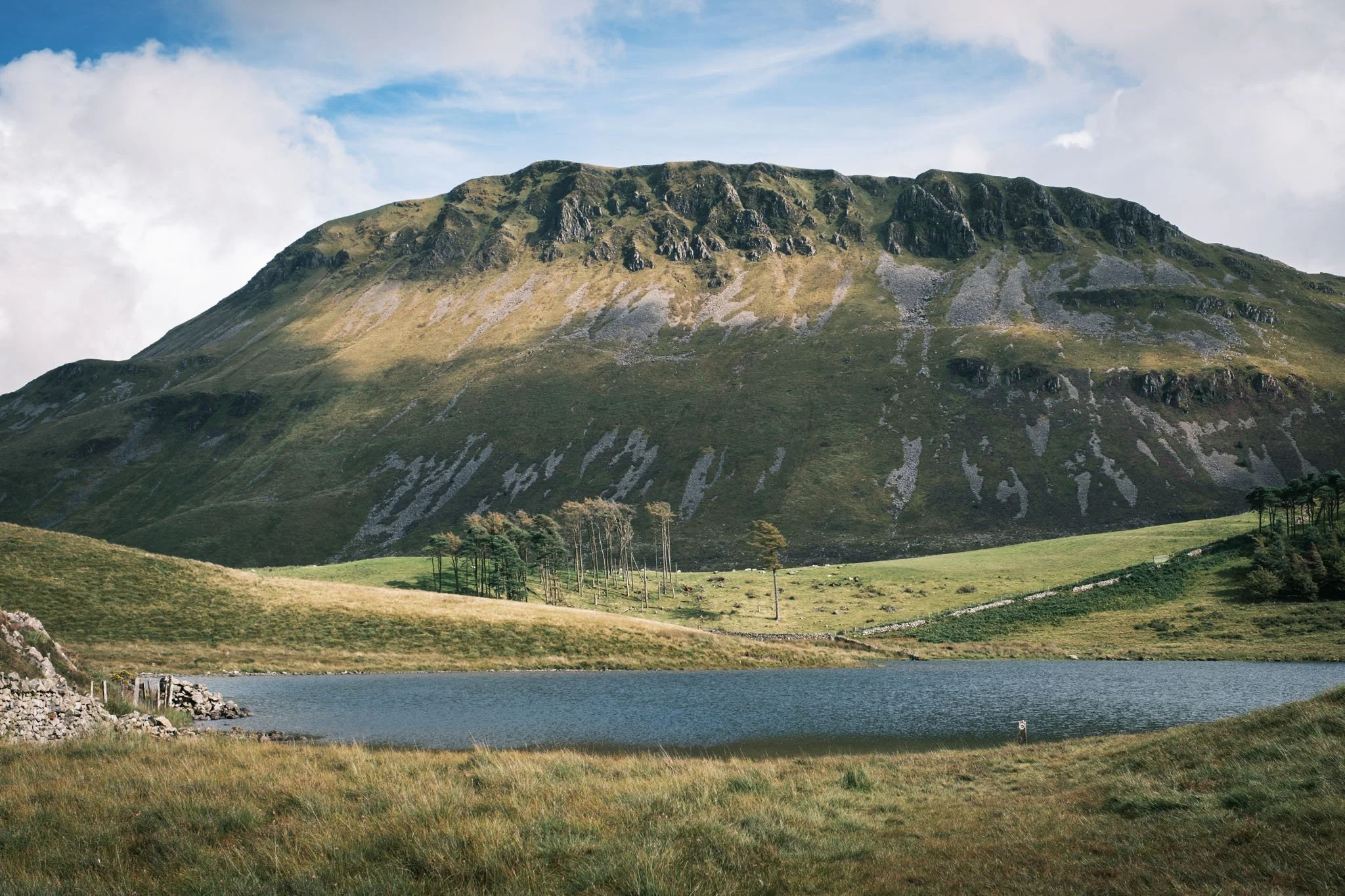 Wales - Green mountain with a lake in the foreground, blue sky, and white clouds.