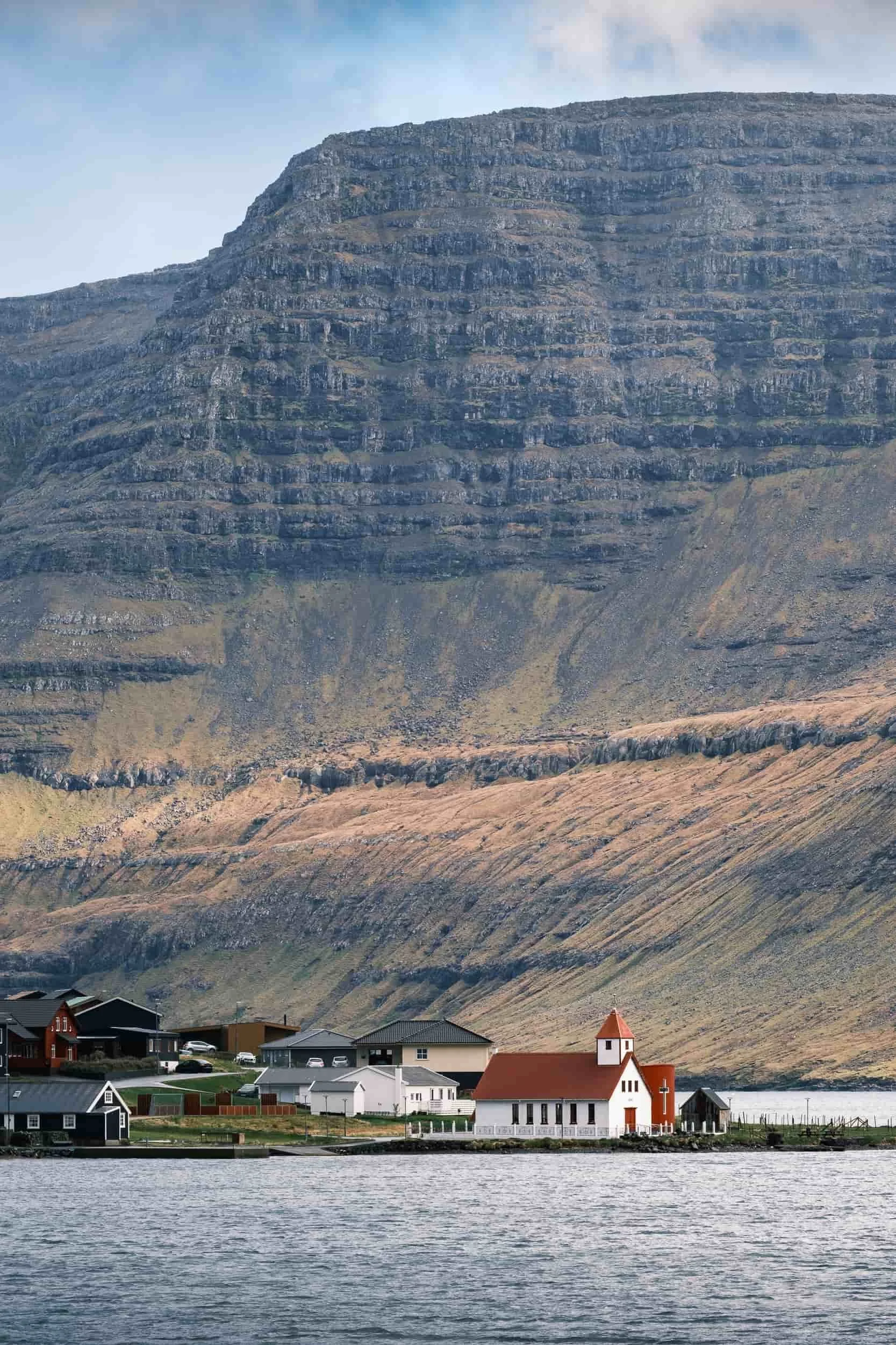 Red church standing in front of an imposing cliff on the edge of a fjord in the Faroe Islands