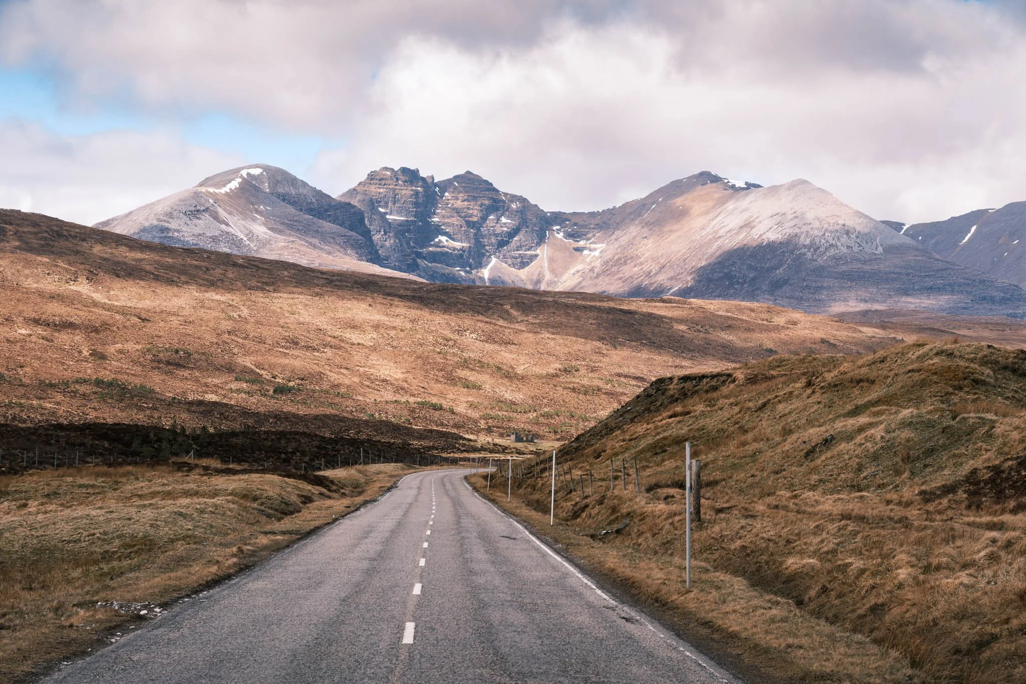 Highland - Scotland - Une route sinueuse dans un paysage de montagne avec des sommets enneigés sous un ciel nuageux.