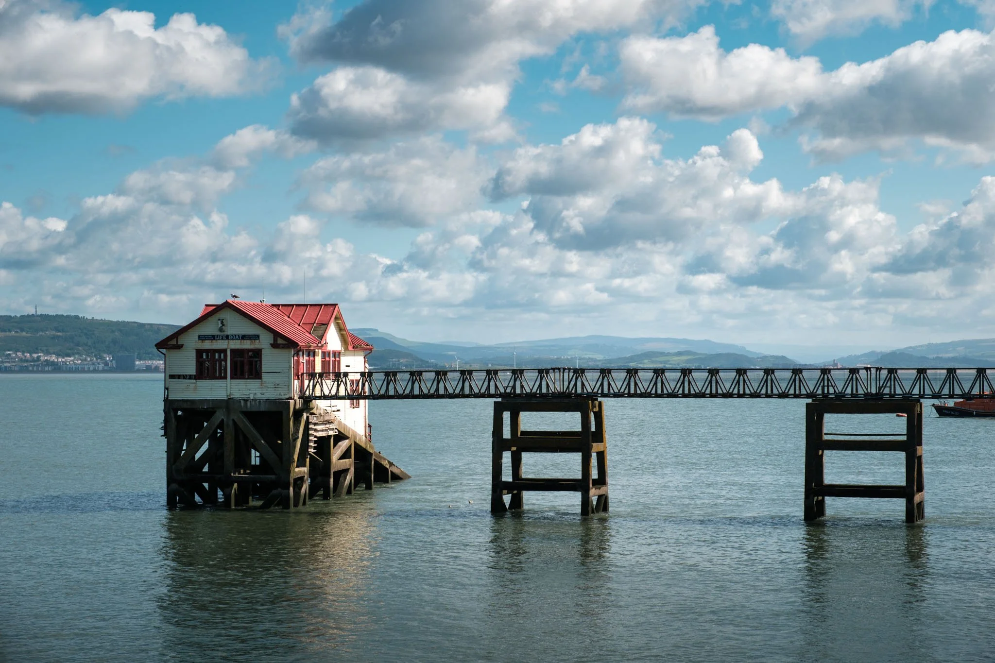 Wales: Fishermen's houses on stilts by the water under a cloudy sky. Outdoor reportage, regional promotion, and sustainable tourism by Guillaume Donsimoni.