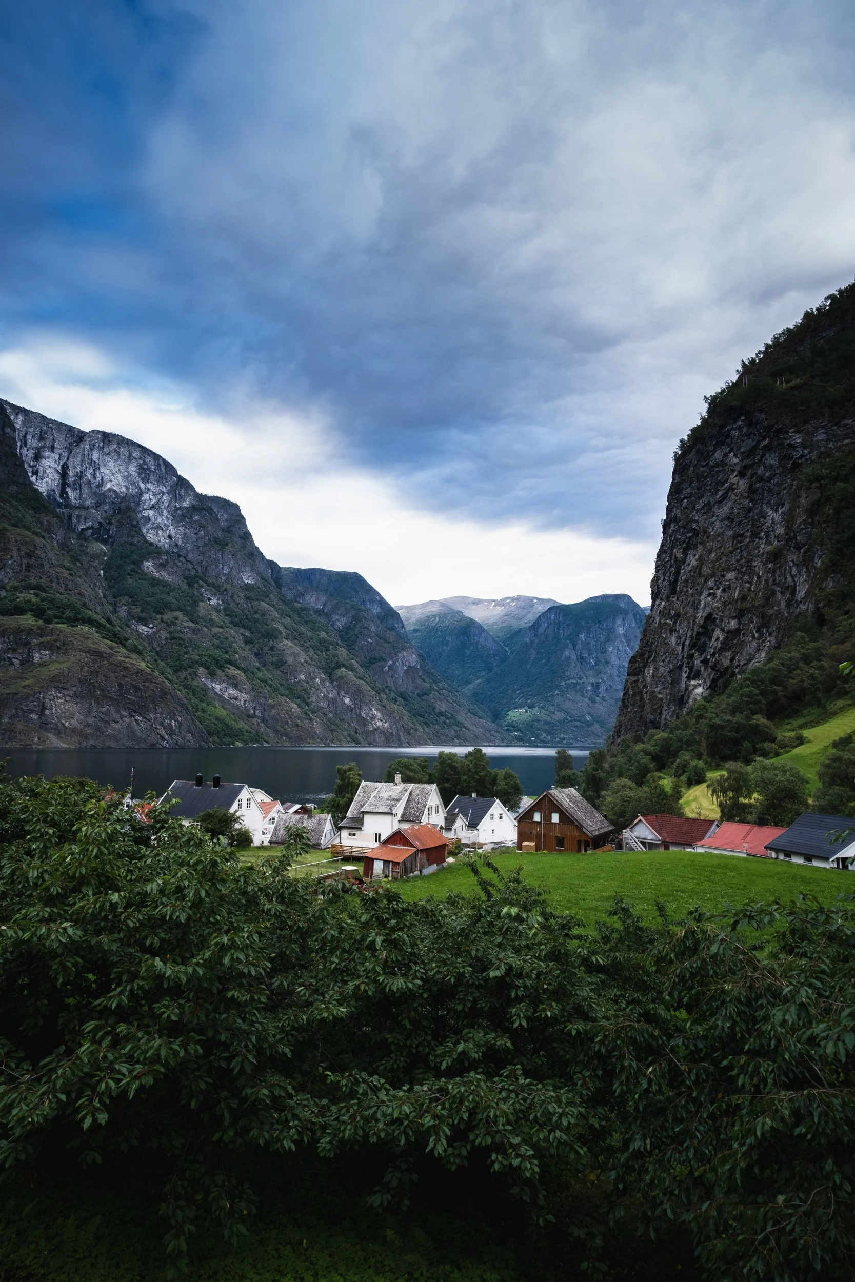 Norwegian village with traditional houses, surrounded by mountains and a lake, under a cloudy sky. Outdoor reportage, territorial promotion, and sustainable tourism by Guillaume Donsimoni.