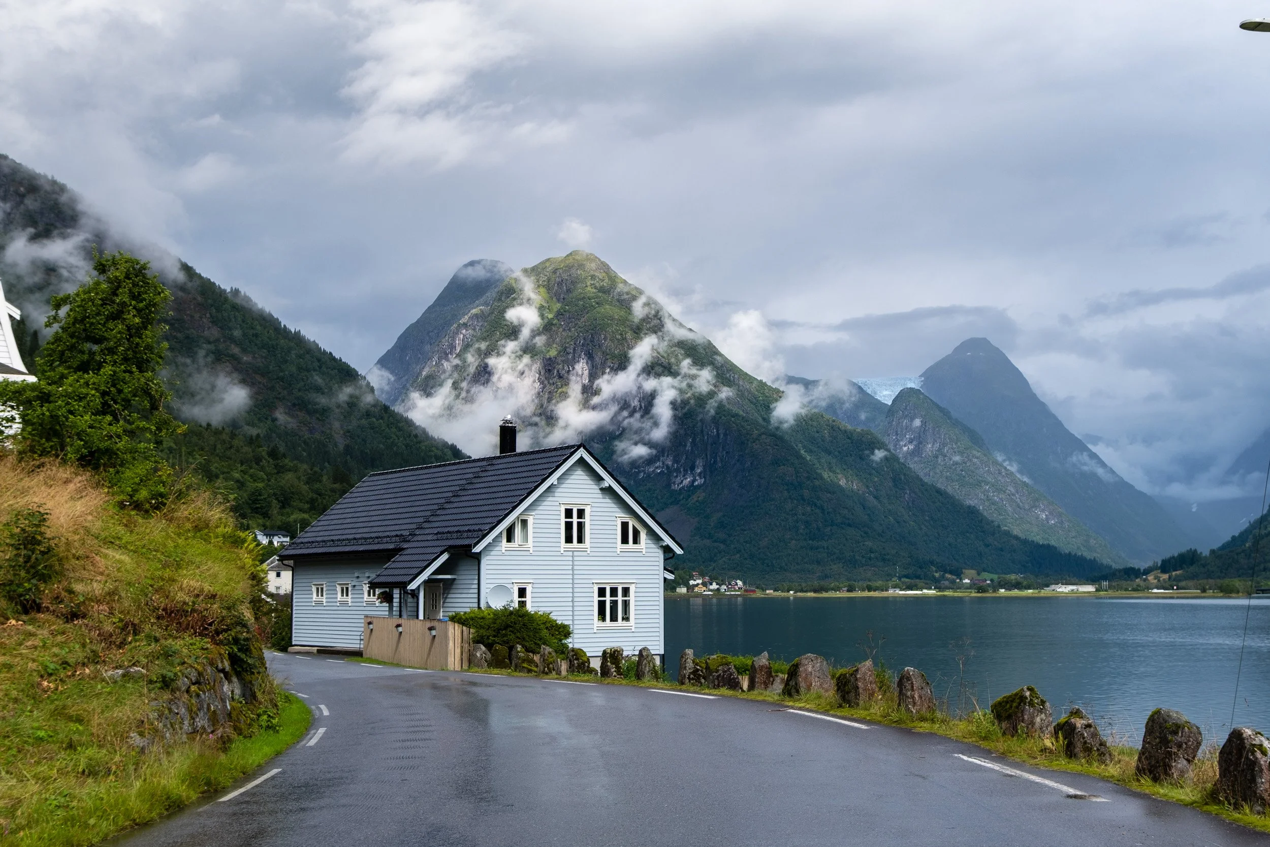 Norway: Wooden houses by a lake surrounded by green mountains and clouds. Outdoor reportage, territorial promotion, and sustainable tourism by Guillaume Donsimoni.