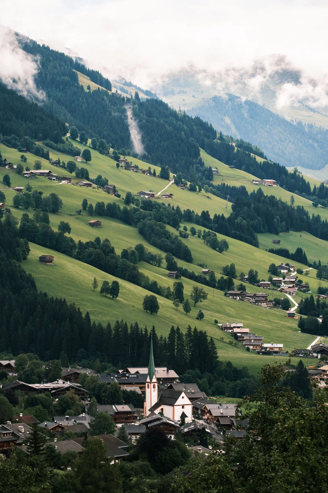 Tyrol - Village avec une église à clocher pointu, entouré de collines verdoyantes et de montagnes brumeuses. Reportage outdoor, mise en valeur du territoire et tourisme durable par Guillaume Donsimoni