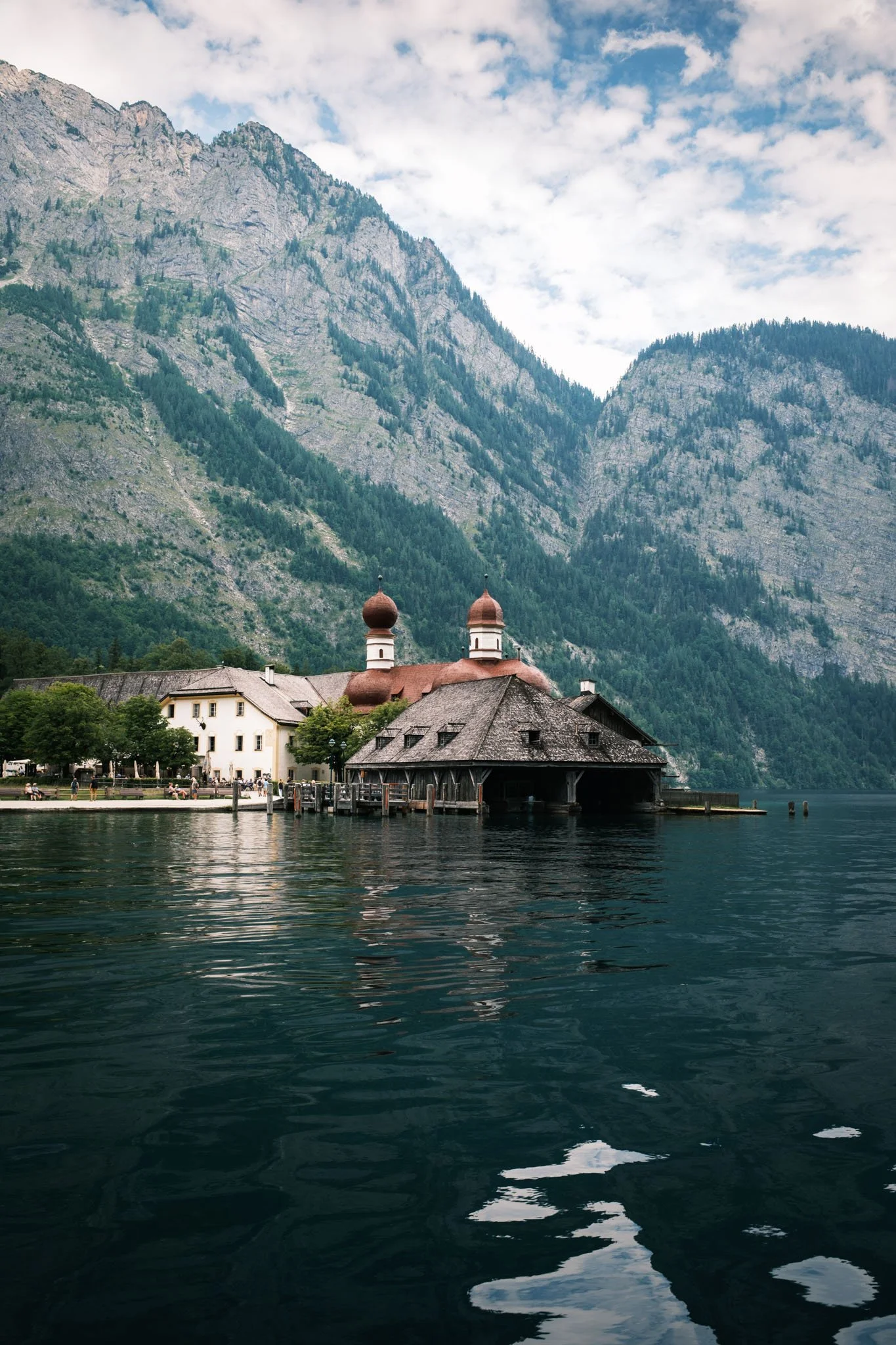 Germany - Bavière - Une maison au bord d'un lac entourée de montagnes avec un ciel partiellement nuageux. Reportage outdoor, mise en valeur du territoire et tourisme durable par Guillaume Donsimoni
