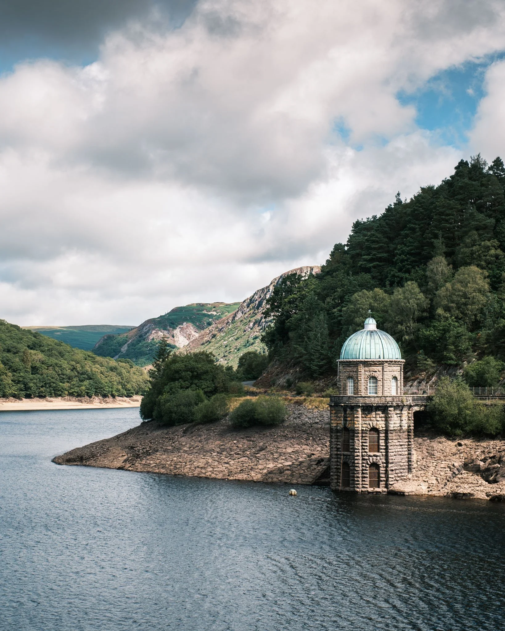 A lake surrounded by lush green mountains and a stone building with a copper dome on the shore. Outdoor reportage, regional promotion, and sustainable tourism by Guillaume Donsimoni.