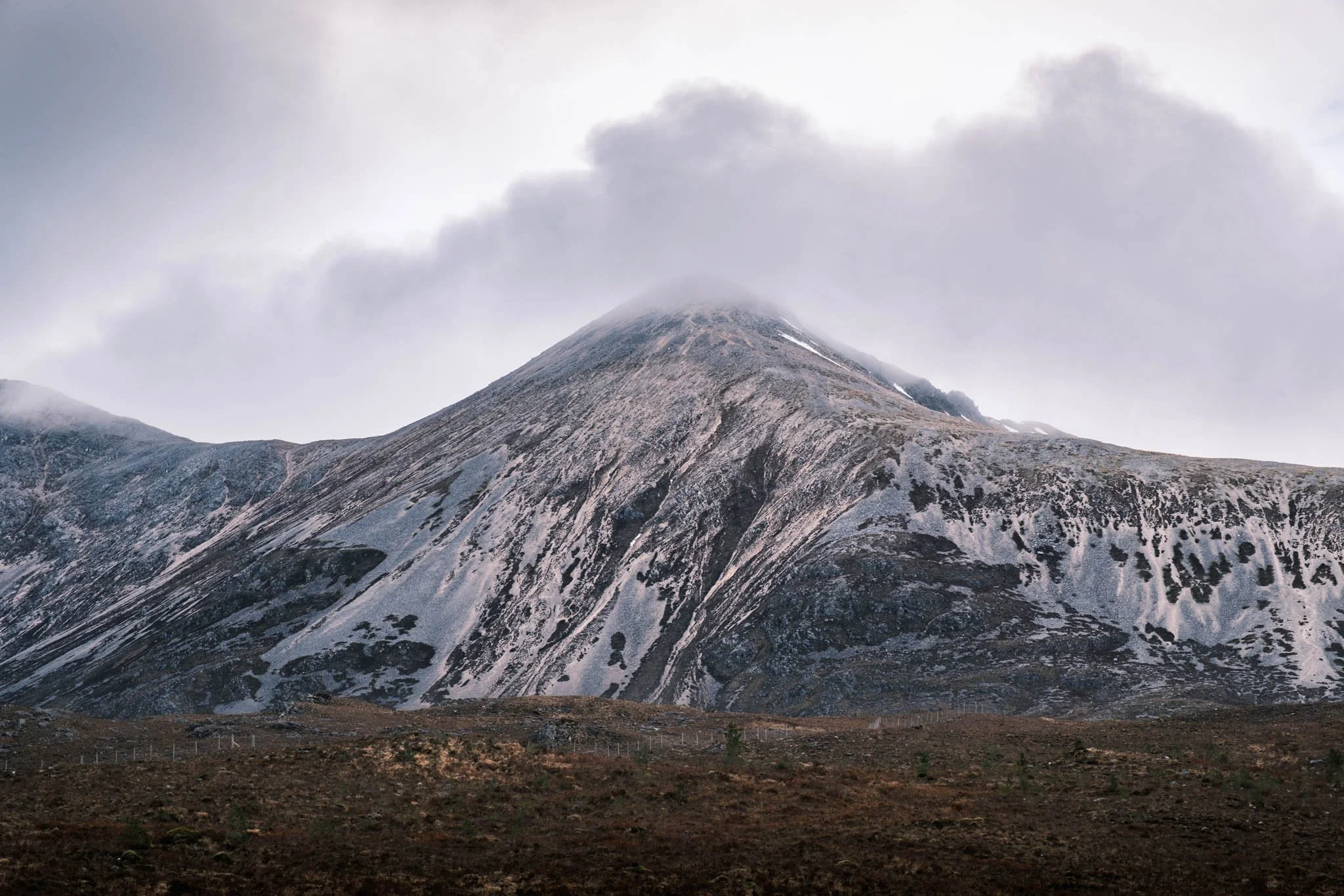 Highland - Scotland - Un sommet de montagne recouvert de neige avec des nuages au-dessus, paysage naturel et rocheux.