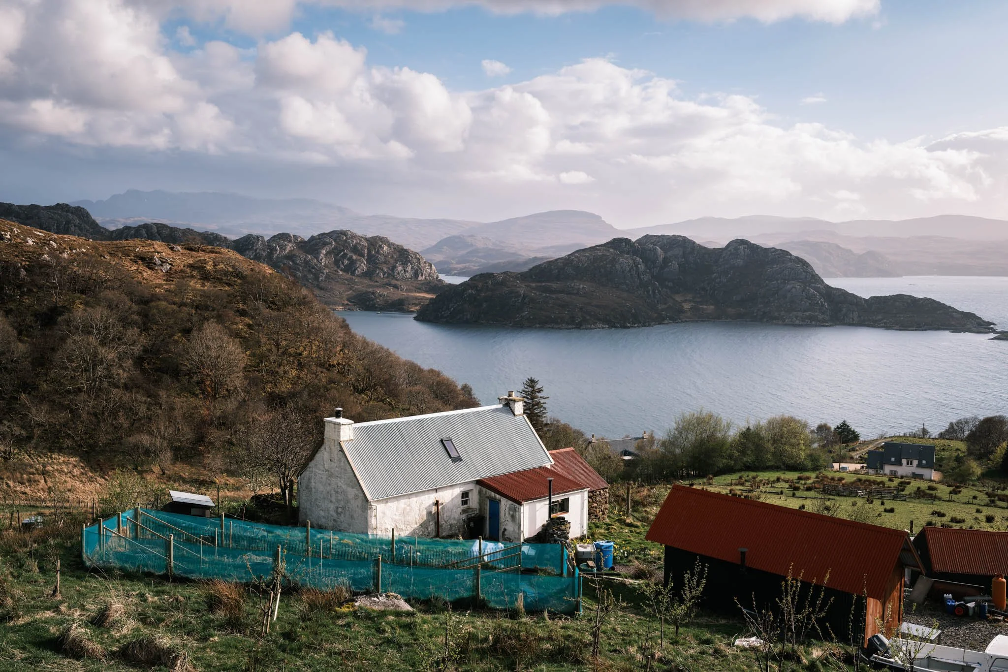 Highland - Scotland - Paysage de montagnes avec un Loch, maisons rurales et ciel partiellement nuageux.