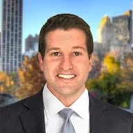 Professional headshot of a smiling man in a suit with a cityscape in the background