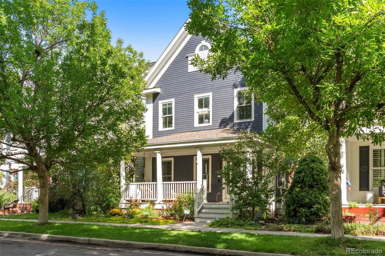 A blue three-story house with white trim and a porch, surrounded by green trees and a well-maintained lawn.
