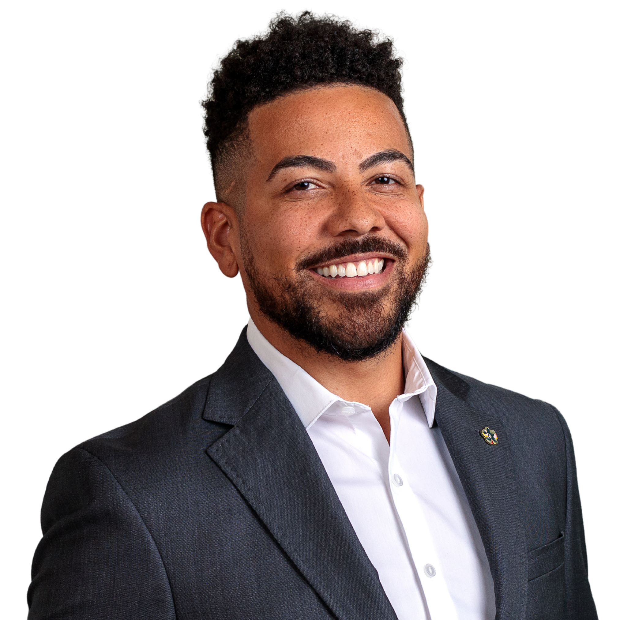 Professional man with short curly dark hair, beard, and brown skin, smiling, in a dark suit and white dress shirt, against a white background.
