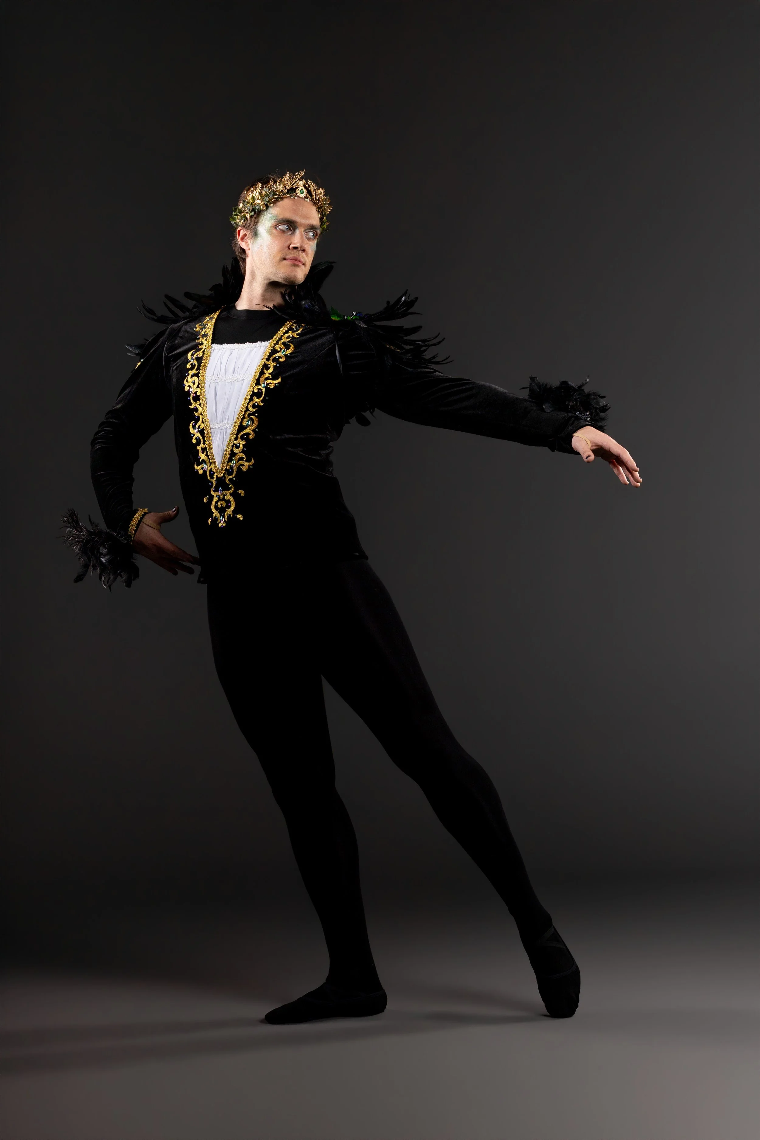 A person performing an aerial dance move, mid-air, in a dark setting, illuminated by a light source. The person is wearing shorts and a T-shirt, with their arms and legs extended dynamically.