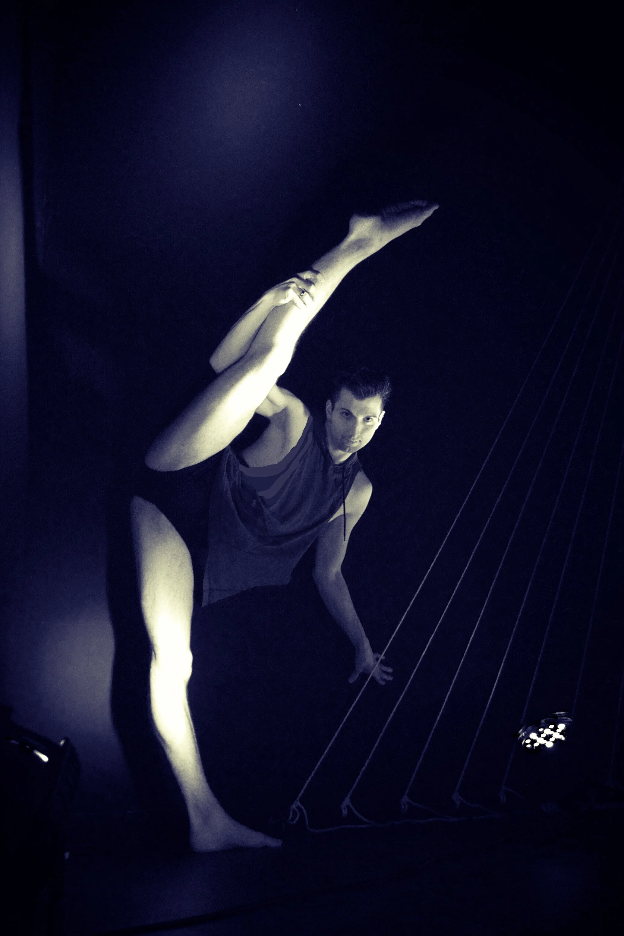 A person in dance attire performing a pose in a dark room with stage lights and rigging.