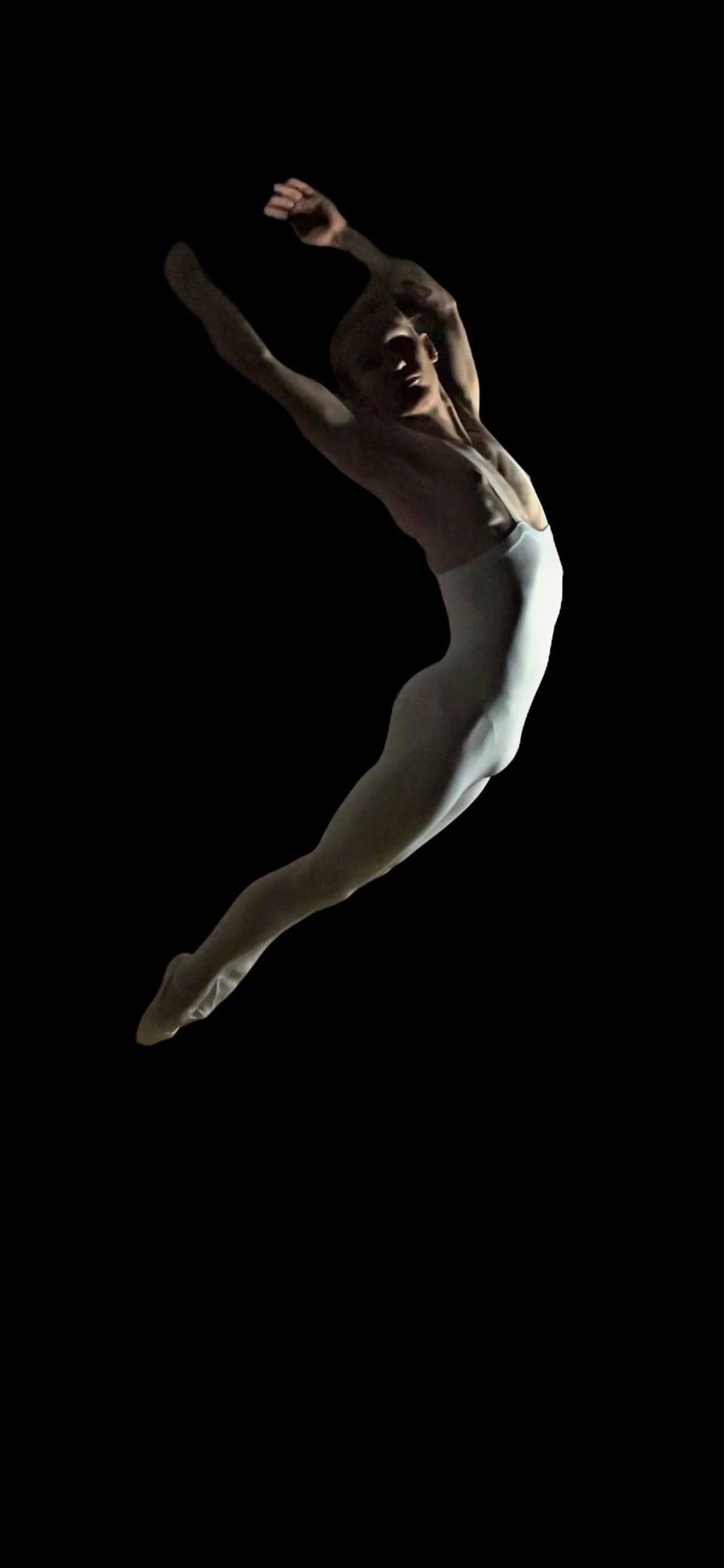 A ballet dancer performing a leap against a black background, wearing white tights and a sleeveless top.