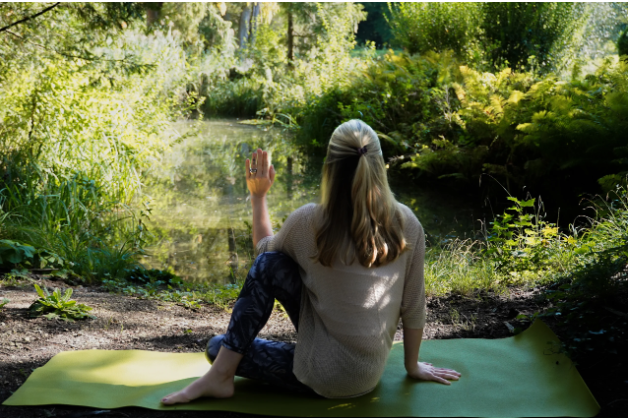 Frau sitzt auf einer Yogamatte am Ufer eines Flusses im Wald und macht eine Meditation oder Yoga-Übung.