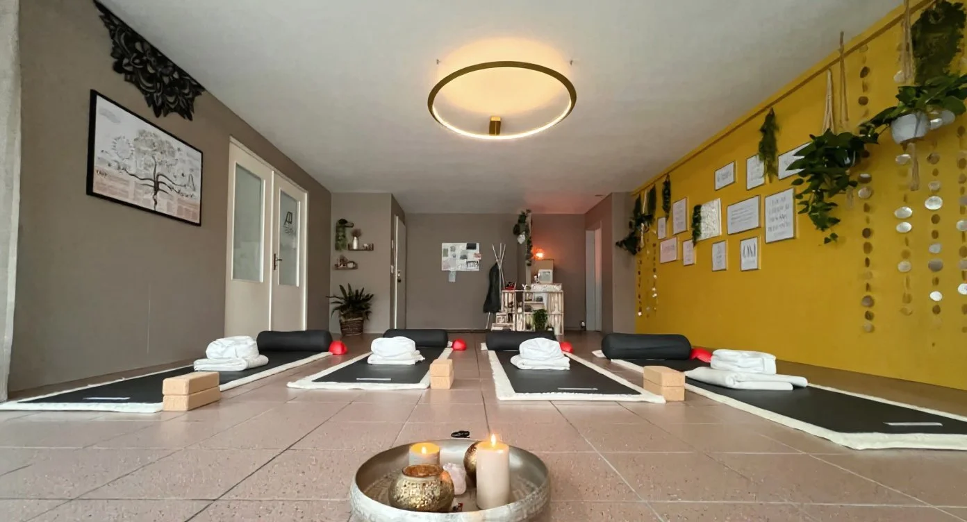 Meditationsraum mit sechs Yoga- oder Meditationsmatten, sorgfältig gefalteten Handtüchern, kleinen geführten Übungshilfen, einer Wanddekoration mit Bildern und Pflanzen, sowie einer Wand mit goldenen Akzenten und Zitaten, ruhige Atmosphäre mit Kerzen im Vordergrund.