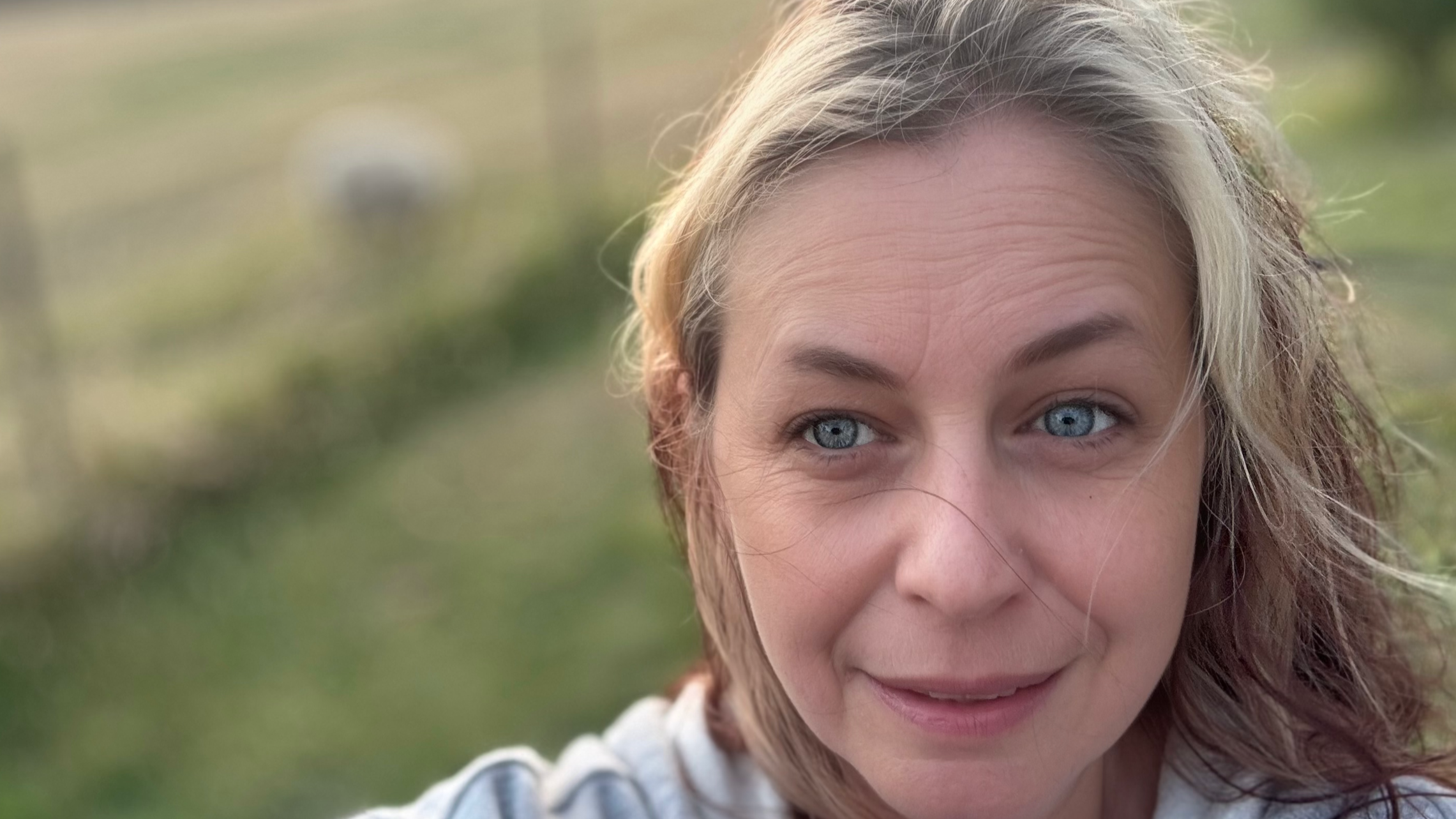 Close-up of a woman's face with blue eyes and blonde hair outdoors.