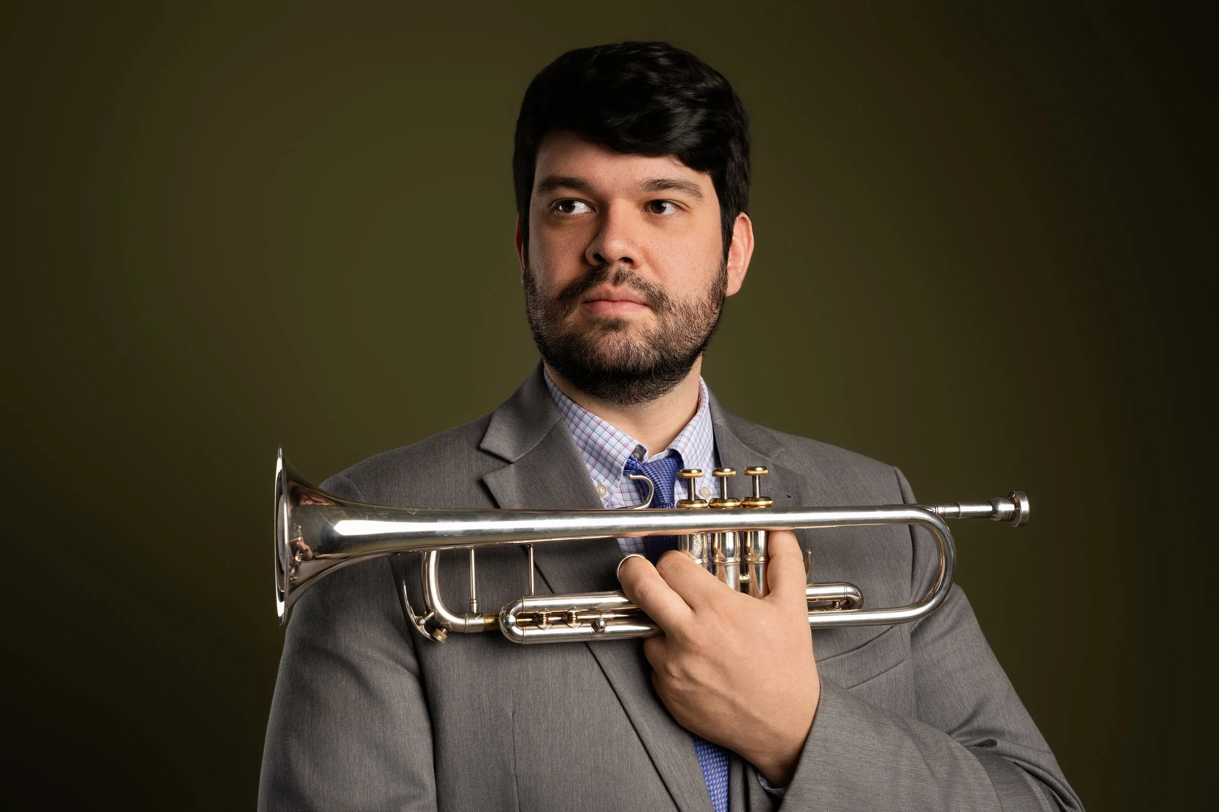 Man in gray suit holding a trumpet against a dark background.