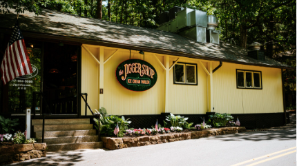 Exterior of Jock's Jock Shop restaurant with yellow siding, stairs, flowers, and an American flag.