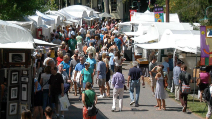 Crowd of people walking through an outdoor market with white tents and booths.