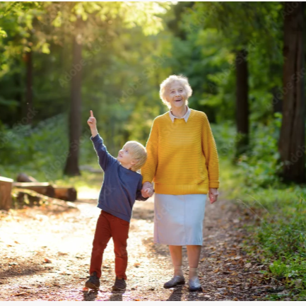 A joyful elderly woman and young boy walking along a wooded trail, holding hands, on a sunny day.
