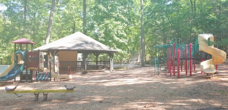 Empty playground with slides, climbing structures, and a gazebo surrounded by trees