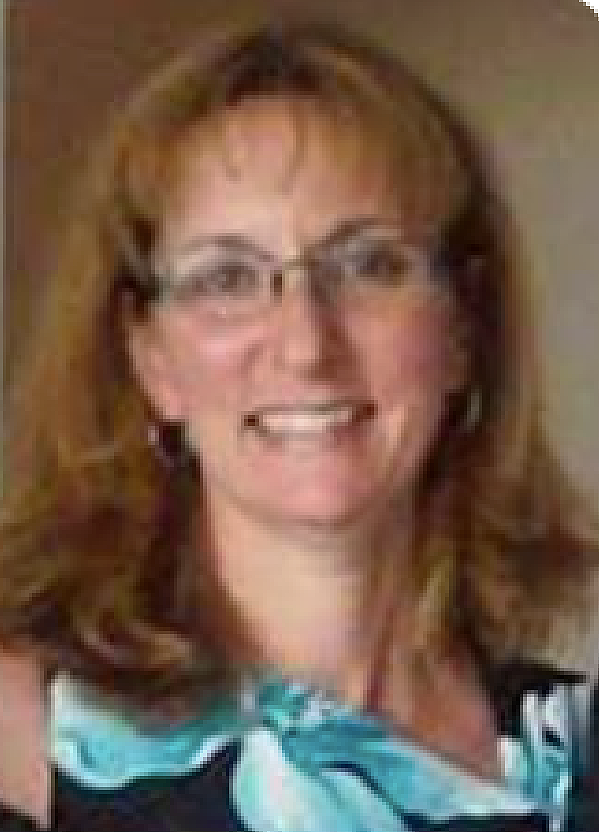 A woman with shoulder-length light brown hair, glasses, and wearing a teal blouse with a black and white pattern, smiling at the camera.