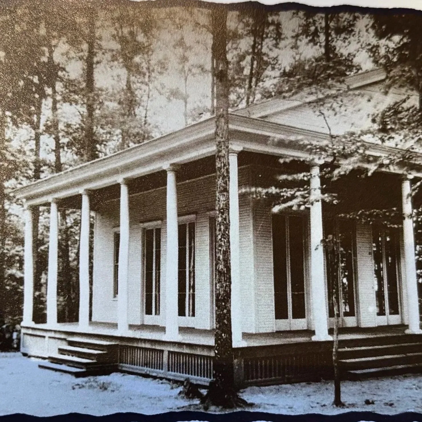 Black and white photo of a large, two-story house with tall, white columns supporting a wide porch roof, surrounded by trees.