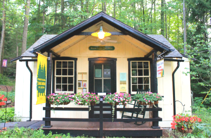 Small white building with black trim, flower planters on the porch, surrounded by trees.