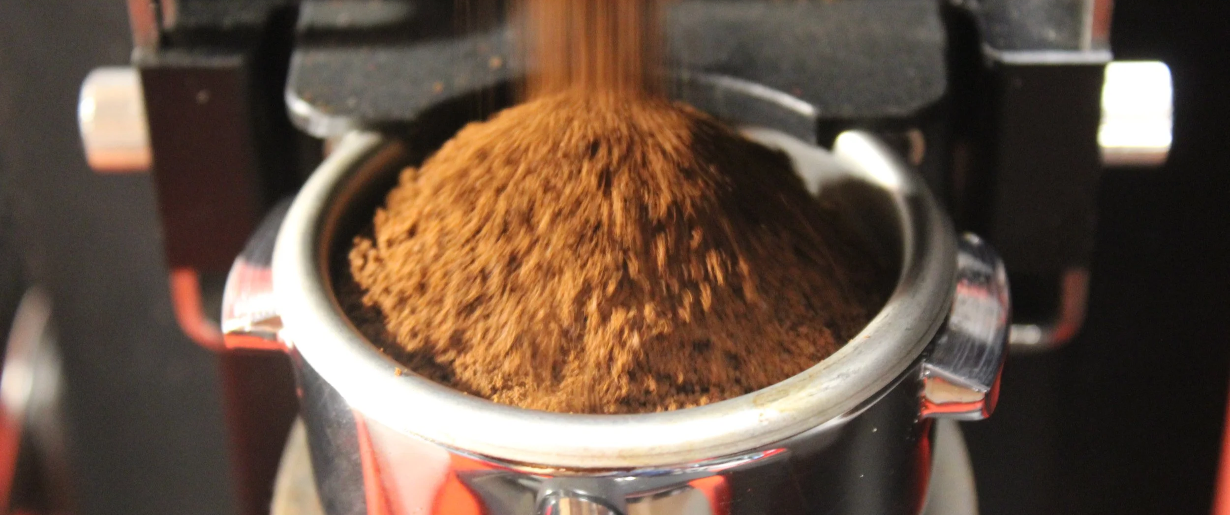 Close-up of freshly ground coffee being dispensed into a portafilter from an espresso machine.