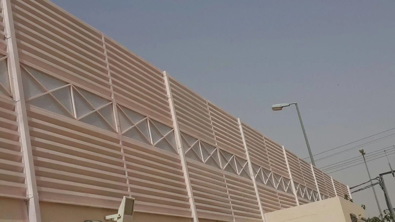 Exterior view of a modern building with pinkish horizontal louvers and a geometric glass window pattern, with a streetlight and electrical wires in the background.