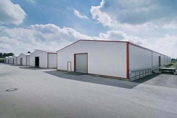 A row of large white storage or warehouse buildings with red trim on a wide paved lot under a partly cloudy sky.