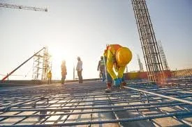 Construction workers on a building site, working with steel rebar, with cranes in the background during daylight.