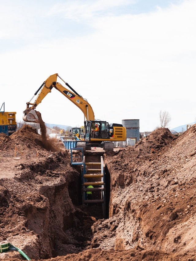 Excavator digging a trench at a construction site with workers nearby.