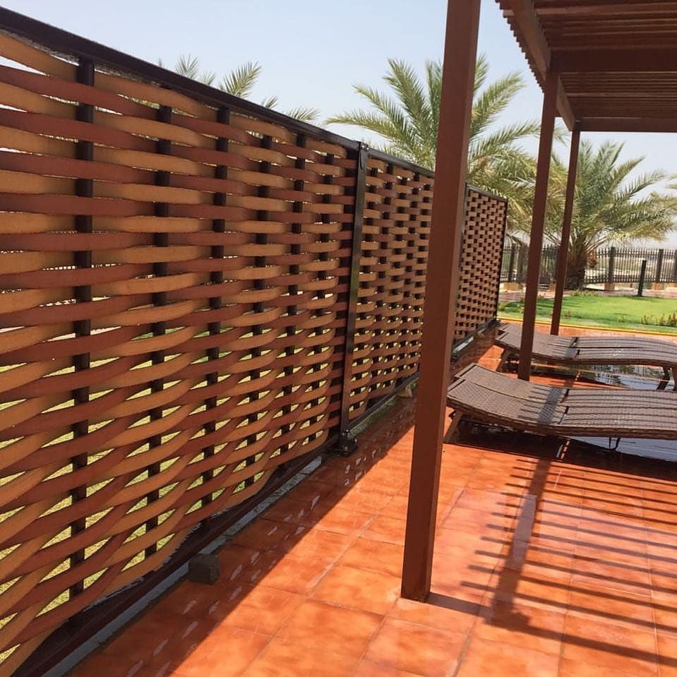 Outdoor patio with wooden lounge chairs, a wooden privacy fence, and palm trees in the background on a sunny day.